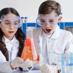 amazed friends in goggles looking at flask with red substance in laboratory