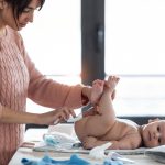 Concentrated young mother changing the nappy to her little son at home.