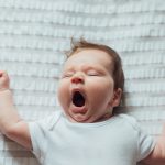 Infant baby sleeping and yawning on white sheets